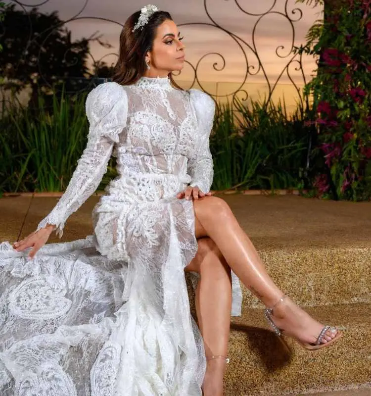 Foto de mulher sentada em escada com vestido de noiva rendado.