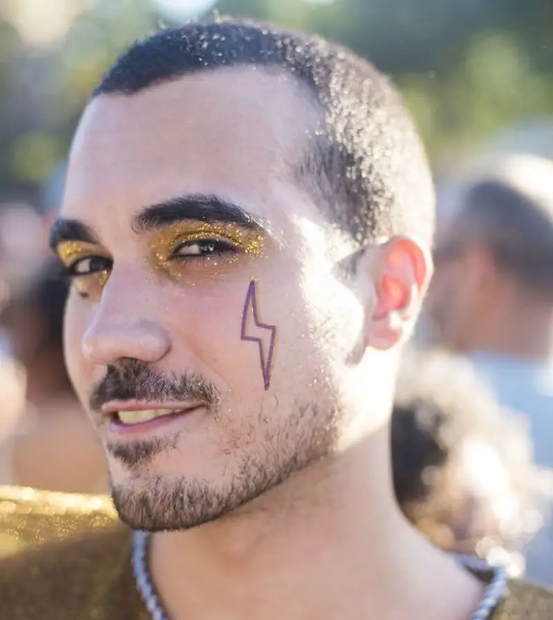 Homem de pele clara com sombra de glitter e raio roxo na bochecha