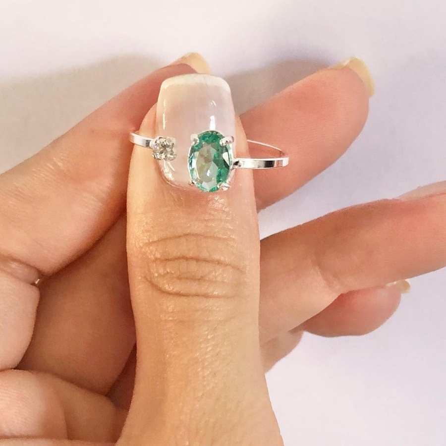 Mulher de pele clara com unha francesinha segurando anel prateado com pedra verde oval