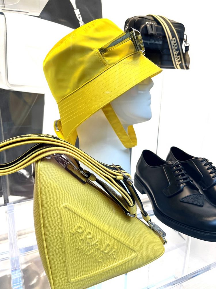 Prada, Milão, verão 2023, amarelo fluor, tendências verão 2023, vitrines de Milão Manequim da marca Prada em Milão usando chapéu amarelo fluor, bolsa ao lado do manequim em amarelo fluor sapato e bolsa preata do lado direito direito da foto