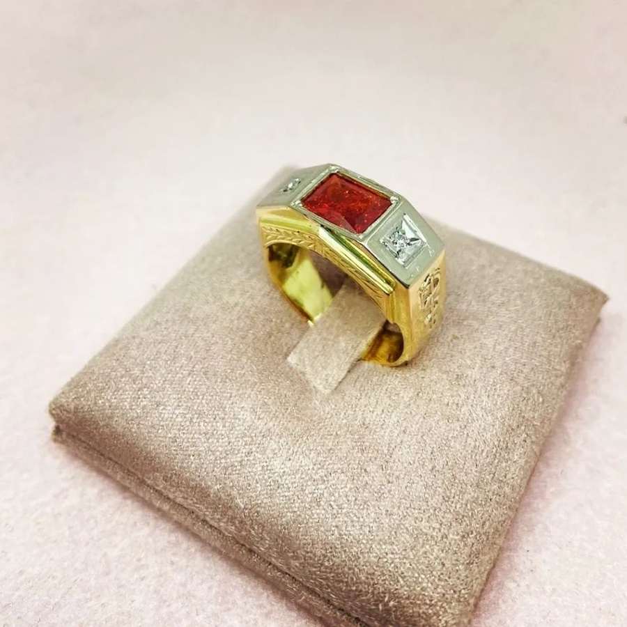 Anel dourado e prateado com pedra vermelha em suporte bege