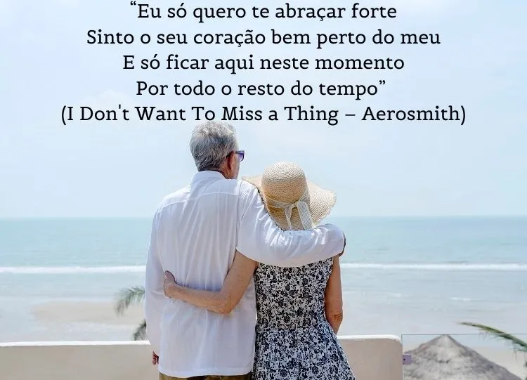 Foto de homem e mulher idosos abraçados na praia e frase: “Eu só quero te abraçar forte / Sinto o seu coração bem perto do meu / E só ficar aqui neste momento / Por todo o resto do tempo” (I Don't Want To Miss a Thing – Aerosmith)