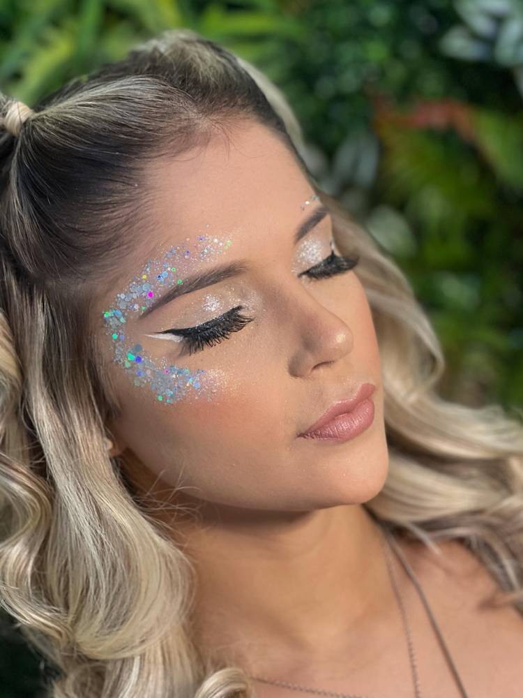 Mulher de pele clara e cabelo loiro com maquiagem simples nos olhos, com delineado e muito glitter próximo aos olhos. 