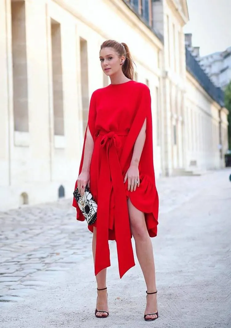 Atriz Marina Ruy Barbosa com vestido vermelho com amarração na cintura, bolsa preta, cabelo preso e salto preto.
