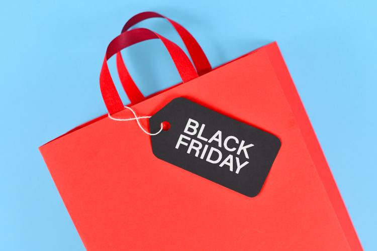 A imagem mostra uma sacola de compras vermelha com alças de fita, sobre um fundo azul claro. Preso à sacola, há um cartão preto com as palavras "Black Friday" em letras brancas. A cena simboliza promoções e compras associadas a essa data especial de vendas.


