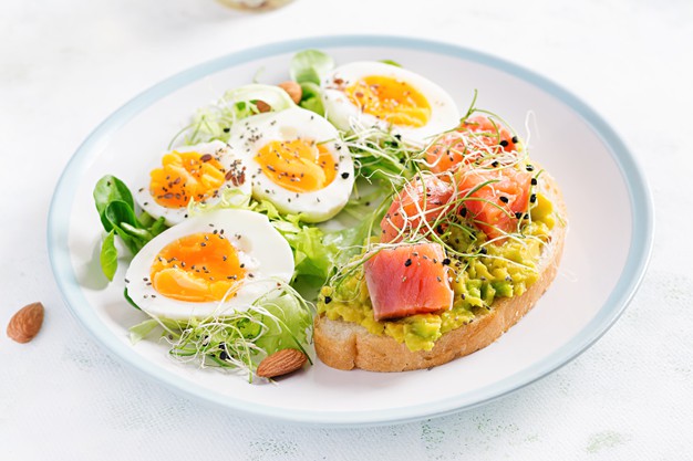 Prato branco com os cozidos, verduras e avocado toast com salmão