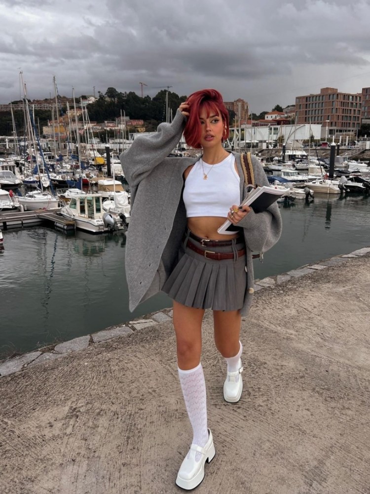 mulher usando regata cropped com saia cinza rodada com sobreposição de cardigan cinza, meia 3/4 branca e sapato branco