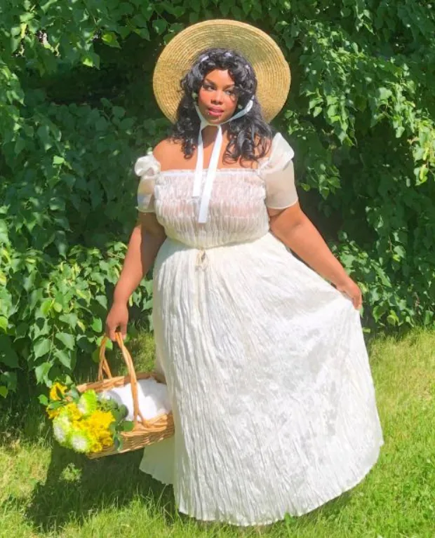 Mulher veste vestido cottagecore branco com chapéu e cesta.