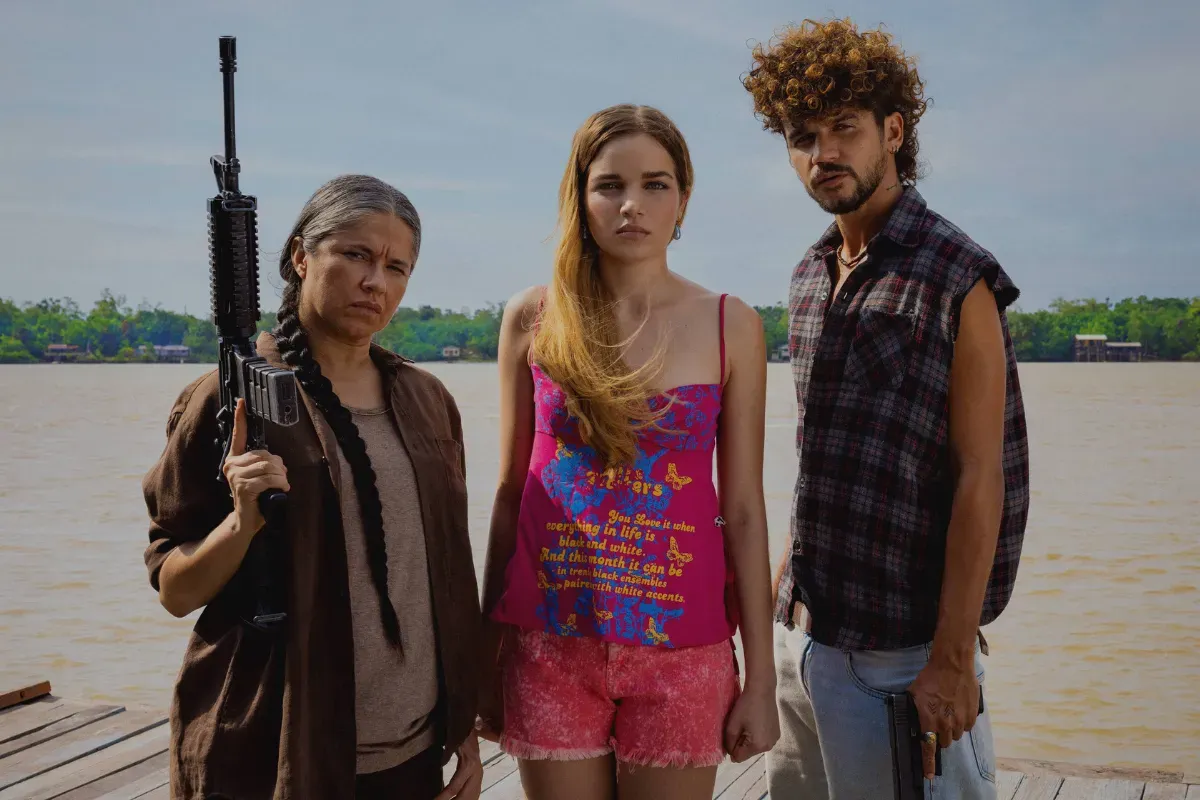 Três personagens de série brasileira em um píer perto do rio com expressão séria