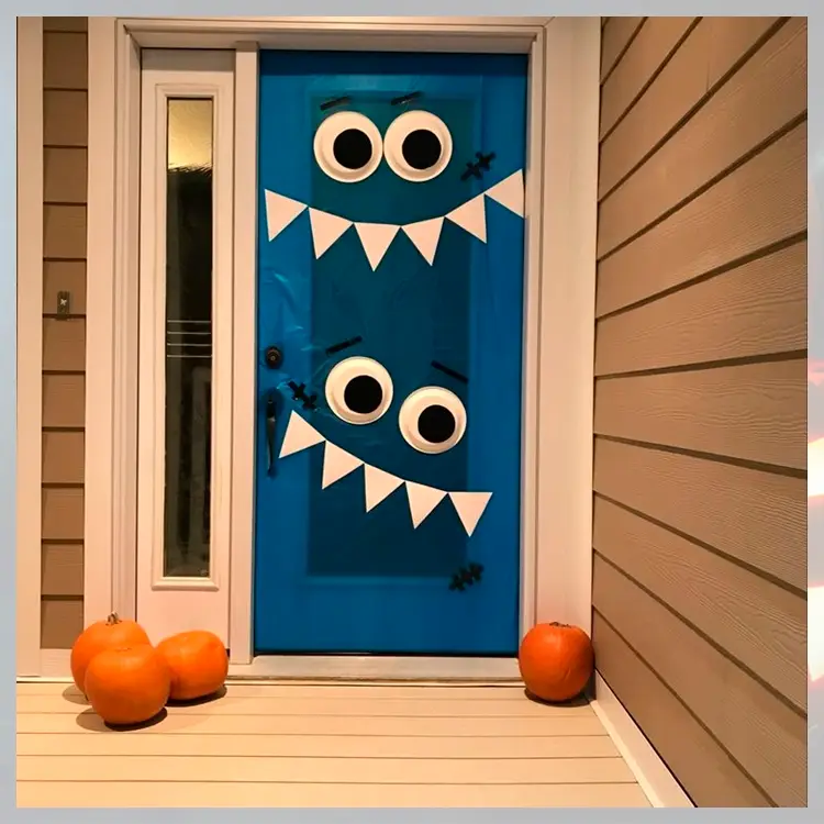 Foto de porta decorada de monstro azul para o Dia das Bruxas, com abóboras no chão 