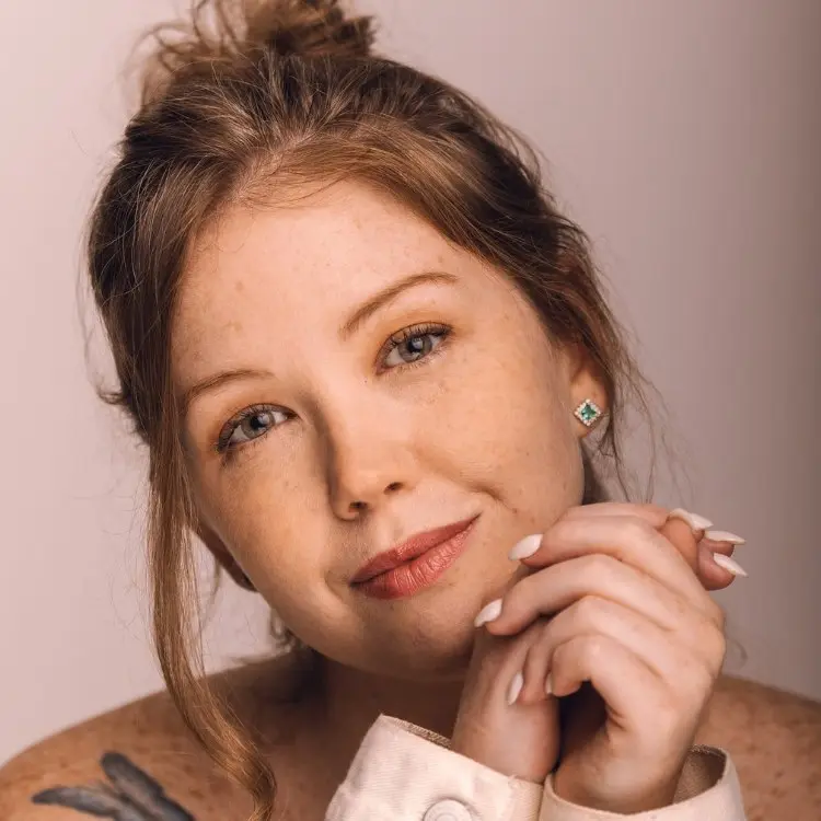 Foto close de Raquel Real, com cabelo preso em coque bagunçado e tatuagem de borboleta no ombro à mostra