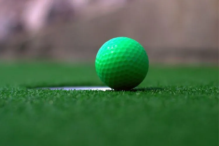 foto de buraco em grama sintética com bola de golfe verde bem na borda
