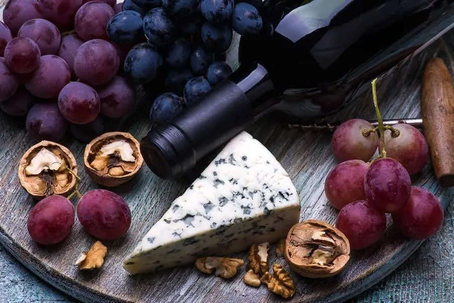 tábua de madeira com garrafa de vinho tinto e aperitivos