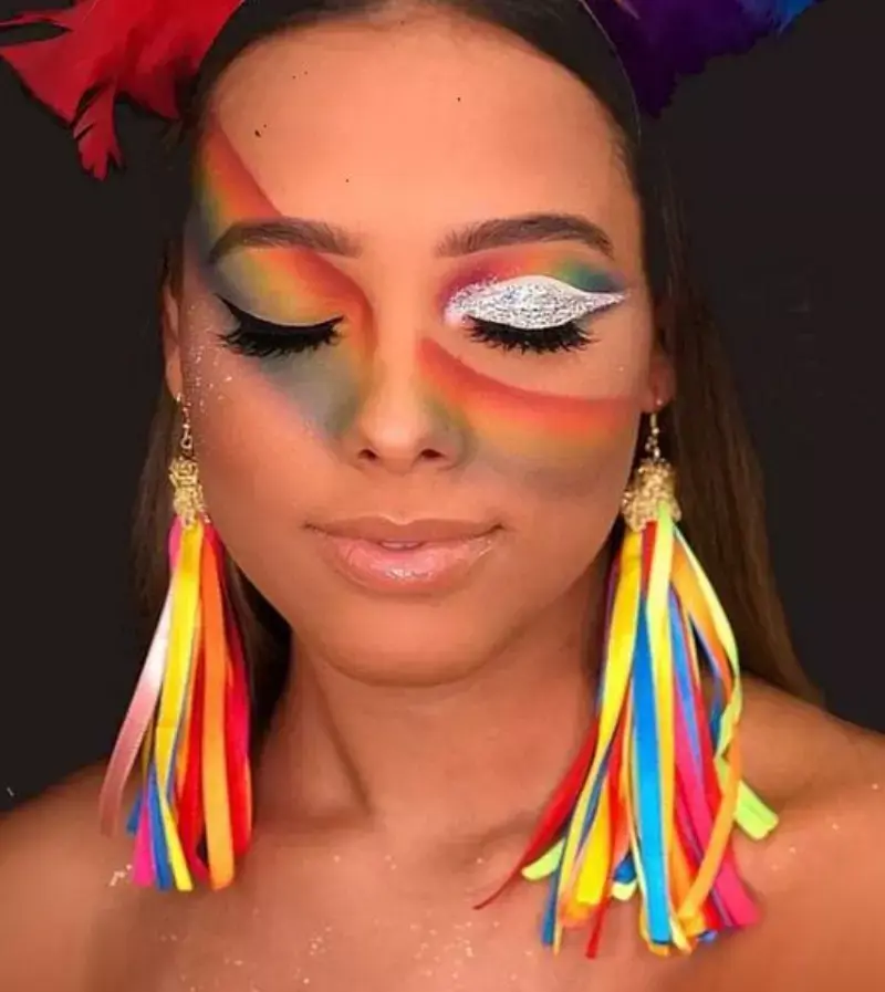 Maquiagem arco-íris com um olho de sombra prateada e brincos fitas coloridas