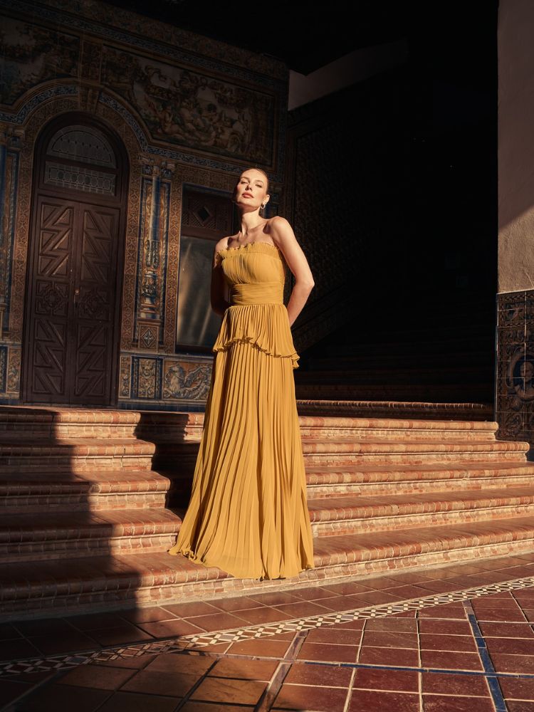 Mulher de pele clara usando vestido longo amarelo-mostarda com babados, plissado e sem alças 