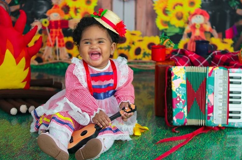 Menina bebê com traje típico de Festa Junina, chapéu, vestido xadrez com renda e babados, e bota 