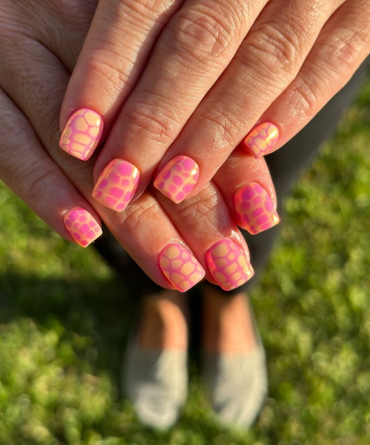 A imagem mostra unhas curtas e quadradas com um design vibrante, perfeito para unhas de carnaval. Elas apresentam um padrão geométrico em tons de rosa e amarelo neon com efeito degradê, destacando um estilo festivo, alegre e ousado.
