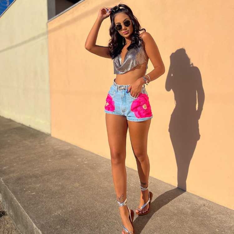 Mulher com look de Carnaval com short jeans de flores rosas e top cropped prateado