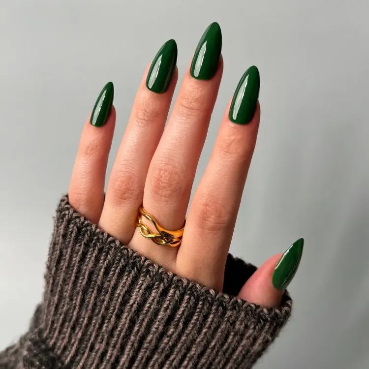 Mão de pele clara com manga marrom e unhas almond verde musgo 