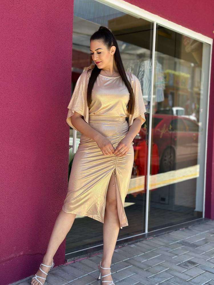 Mulher de pele clara e cabelo escuro usando look de ano novo dourado, com saia midi com fenda e blusa de manga larga.