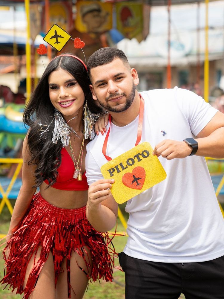 Mulher usando tiara de avião e homem usando plaquinha de Carnaval de piloto