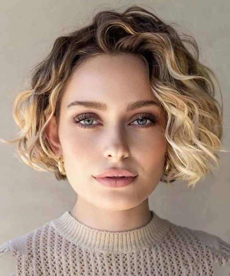 Mulher com cabelo loiro ondulado, raiz morena e corte curto repicado