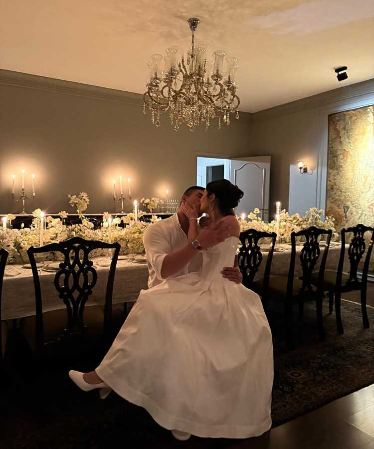 Casal Franciny Ehlke e Tony Maleh celebra os casamentos de famosos 2025 com beijo romântico em cerimônia íntima. Noiva veste vestido branco elegante, e noivo traja camisa branca descontraída. Mesa decorada com flores brancas e candelabros ilumina o ambiente sofisticado e acolhedor.
