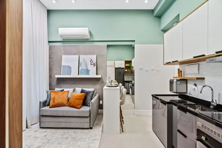 Sala de parede verde com sofá cinza, tapete, integrada com cozinha 