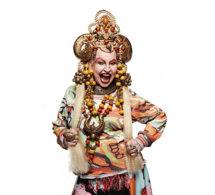 Foto colorida de Elke Maravilha mais velha posando para a campanha de inverno 2015 da grife mineira Lucas Magalhães com uma roupa muito colorida, peruca loira muito longa, muitos acessórios, e um adorno na cabeça com chifres. Elke Maravilha posando para a campanha de inverno 2015 da grife mineira Lucas Magalhães com uma roupa muito colorida, peruca loira muito longa, muitos acessórios, e um adorno na cabeça com chifres.