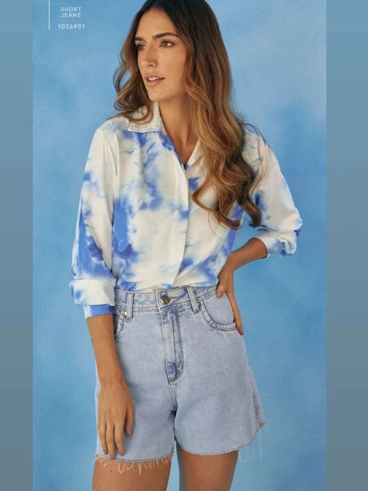 Mulher de pele clara com camisa branca e azul, além de shorts jeans