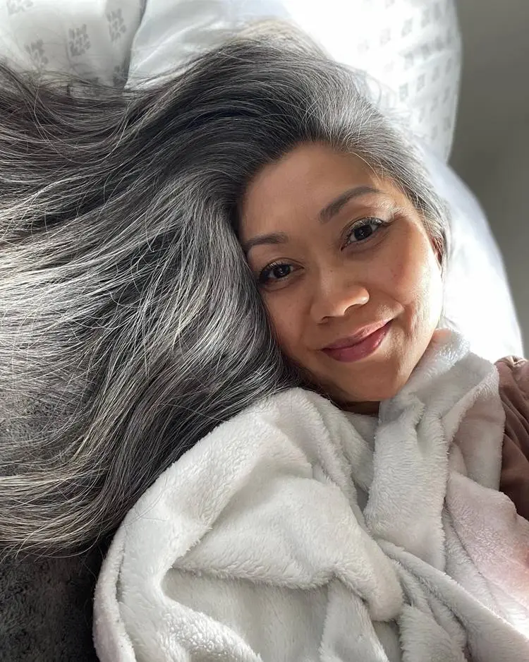 Mulher oriental com cabelo liso grisalho deitada na cama