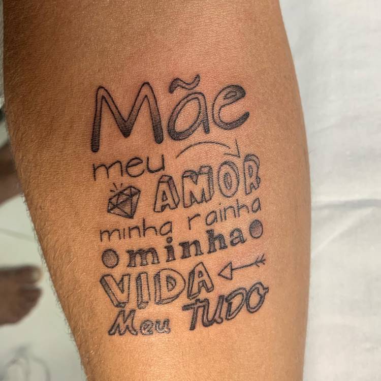 A imagem apresenta uma tatuagem no antebraço de uma pessoa com a palavra "Mãe" destacada. Abaixo, frases como "meu AMOR", "minha rainha", "minha VIDA" e "Meu TUDO" são escritas com diferentes fontes e alguns símbolos, como um diamante e setas. A tatuagem é em preto.







