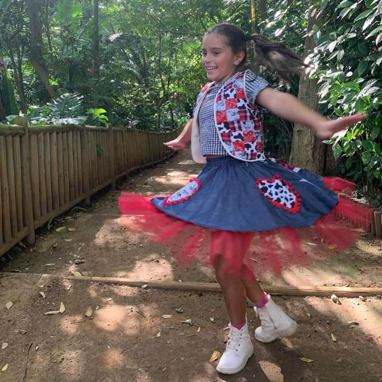 Menina usando cropped xadrez, saia e colete com estampa de vaquinha para festa junina.
