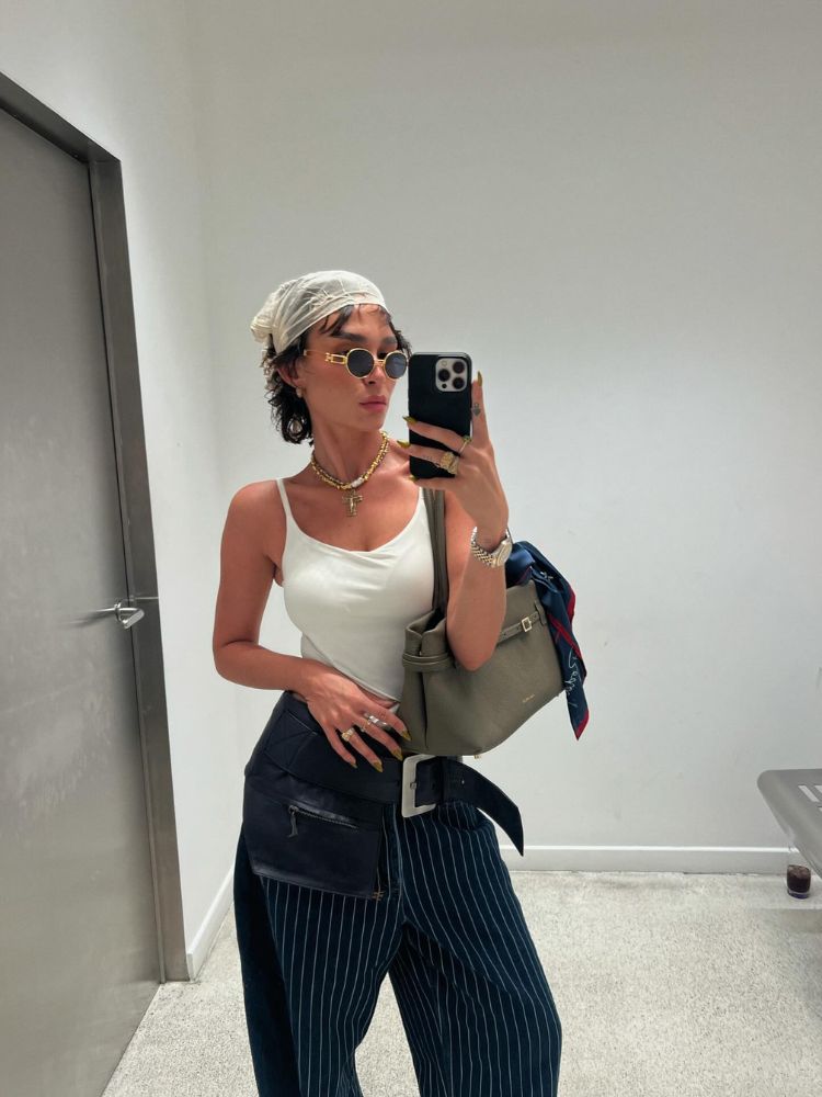 Mulher de pele clara usando bandana de renda, regata branca e calça azul lápis com maxi cinto