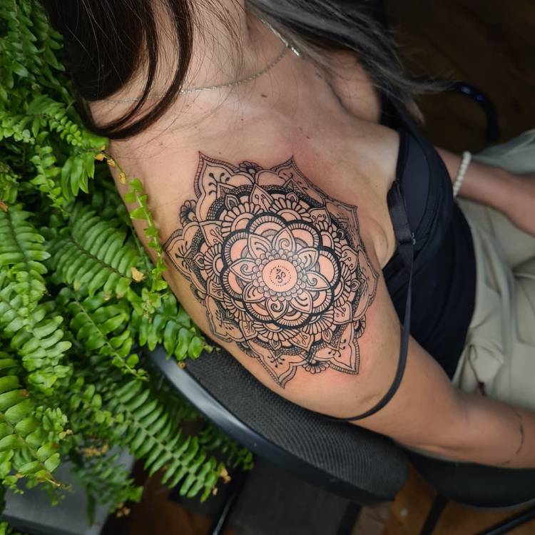Mulher de pele clara usando corset preto e calça jeans, com uma tatuagem de mandala sombreada no ombro