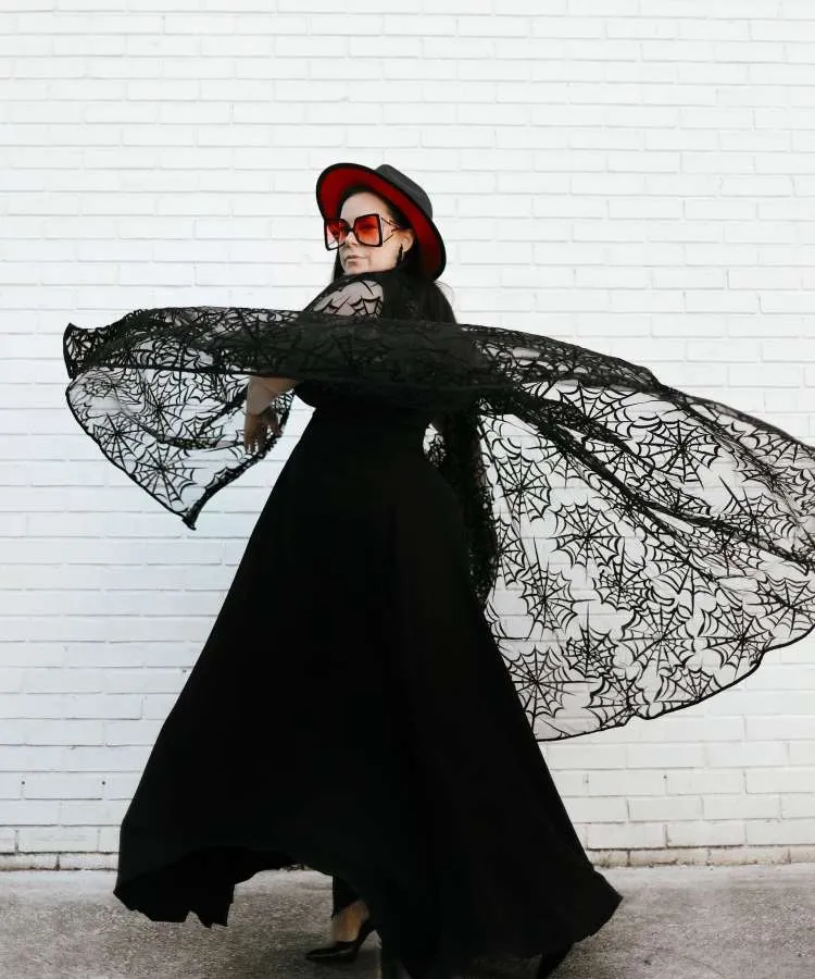 Mulher com vestido preto, capa de teia de aranha, chapéu preto e vermelho