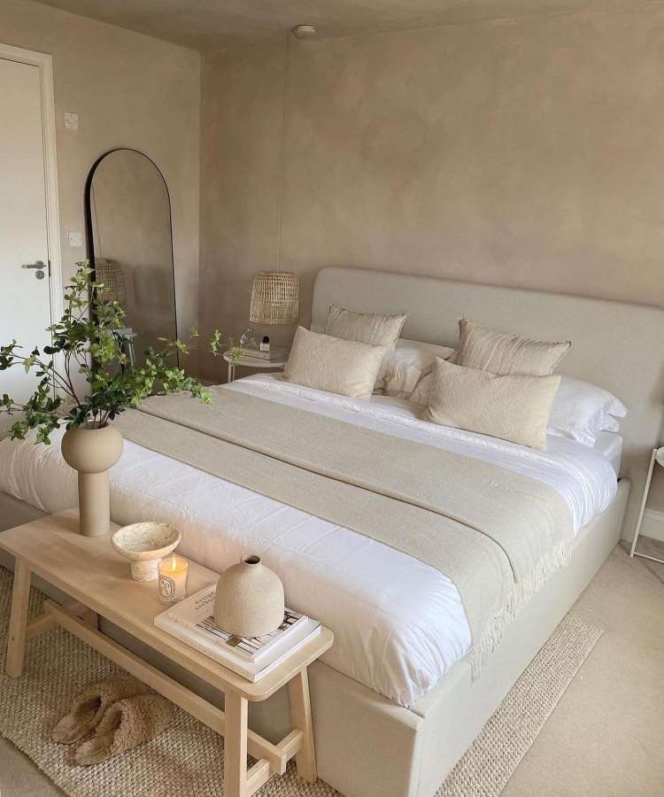 Quarto de casal com espelho oval apoiado em parede. Cores predominantes: off-white e branco