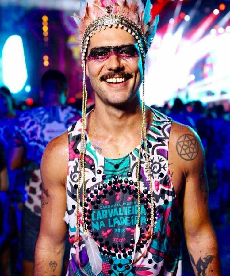 Homem com maquiagem de glitter e coroa de índio para o Carnaval, com "máscara" de glitter preta e rosa