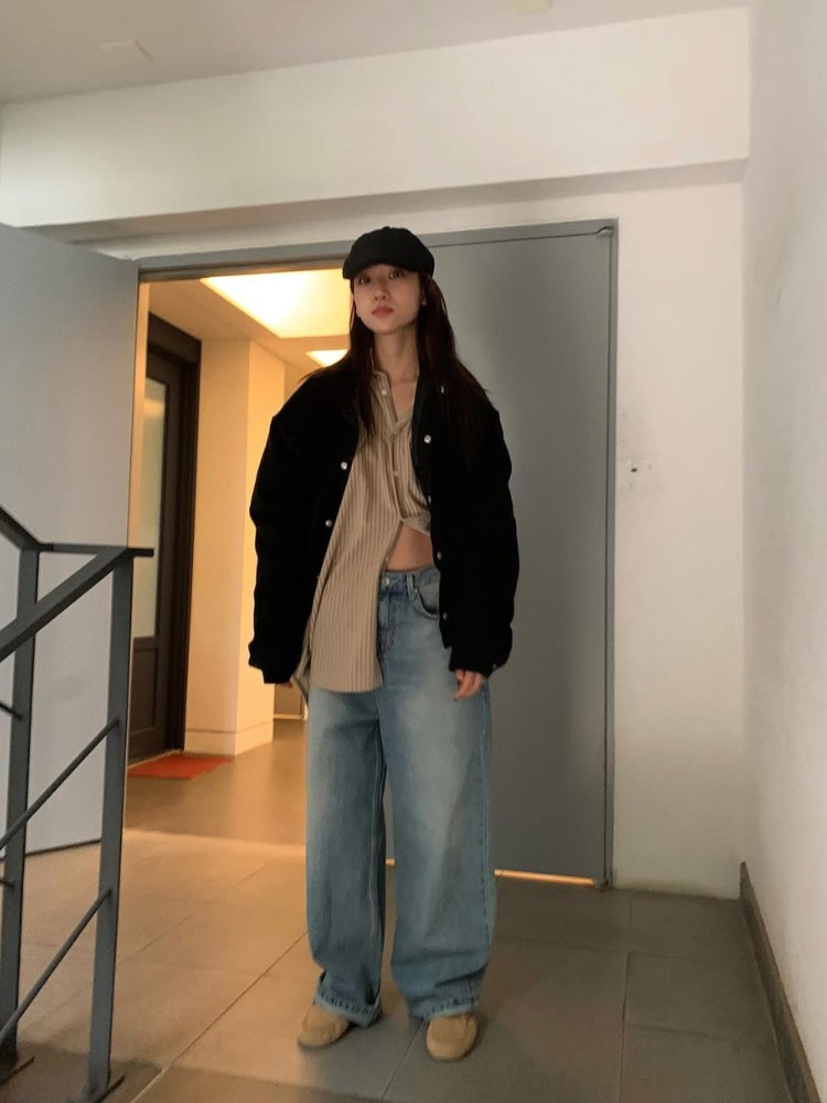 Mulher de origem asiática usando camisa bege, jaqueta preta, calça jeans, mocassim bege 