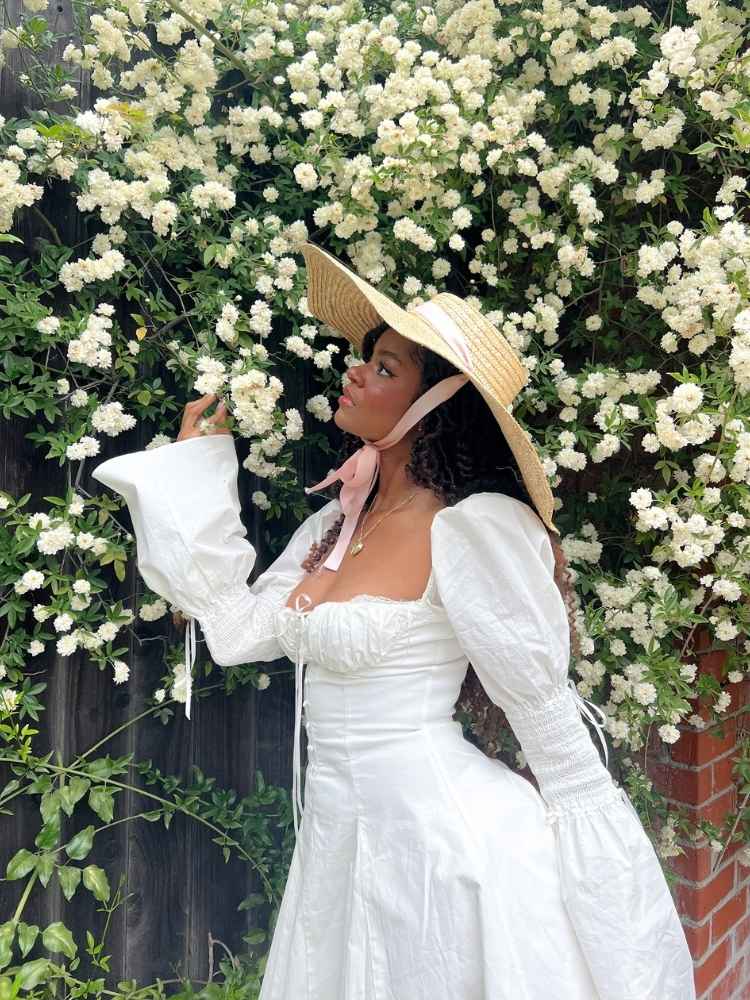 Mulher de pele negra com vestido cottagecore com manga bufante e chapéu de palha 