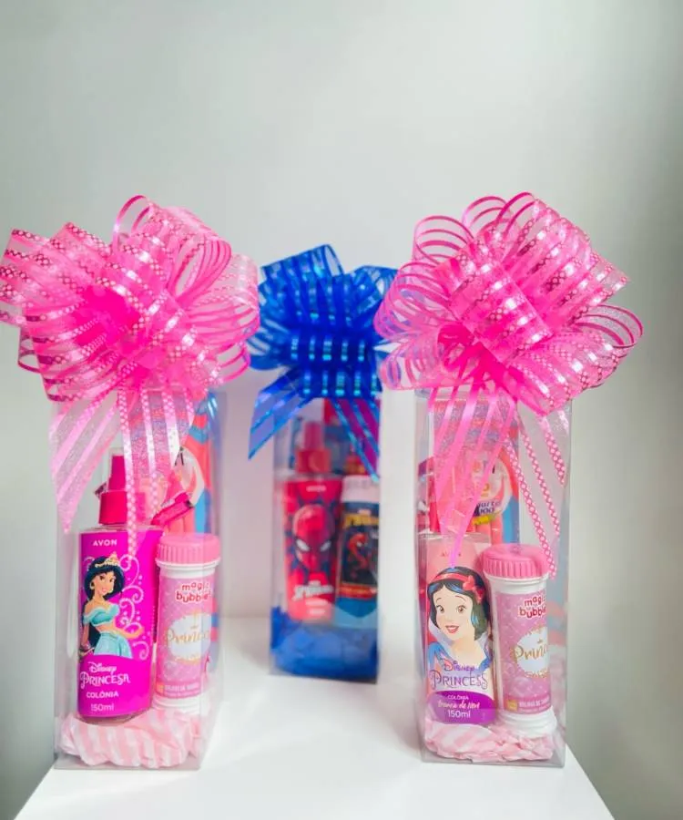 Três kits de banho embalados em caixas transparentes e com laços grandes e coloridos. Os kits são temáticos, com produtos de princesas Disney como Jasmine e Branca de Neve, e do Homem-Aranha.

