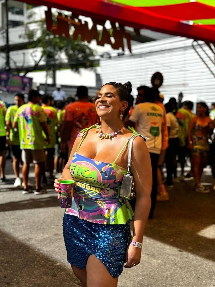 Mulher de pele morena usando abadá colorido como blusa de alcinha e saia azul com brilho