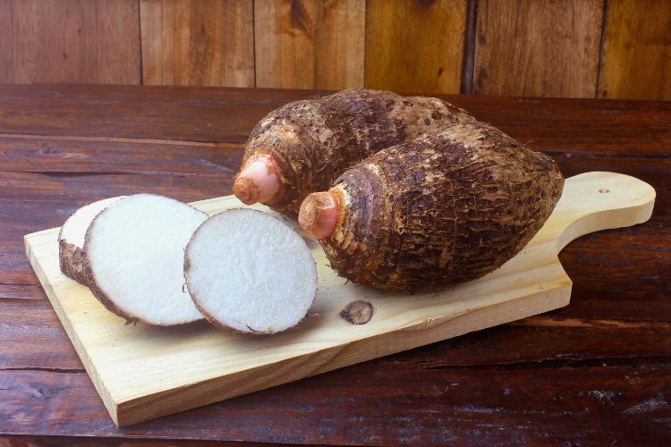 Inhames inteiros e em rodelas sob uma tábua de madeira que está em uma mesa de madeira rústica