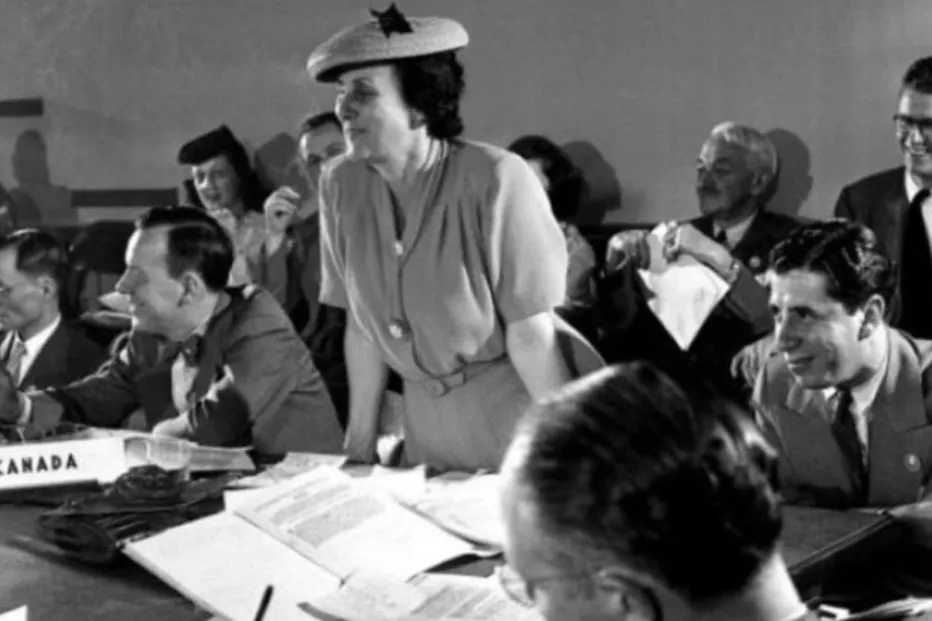 Foto em preto e branco de Bertha Lutz na assinatura da Carta da ONU, em pé debruçada sobre a mesa e rodeada por homens Bertha Lutz representando o Brasil na assinatura da Carta da ONU, em 1945.