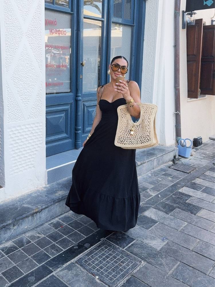 Mulher de pele clara usando vestido preto, bolsa de palha e óculos aviador de lente amarela