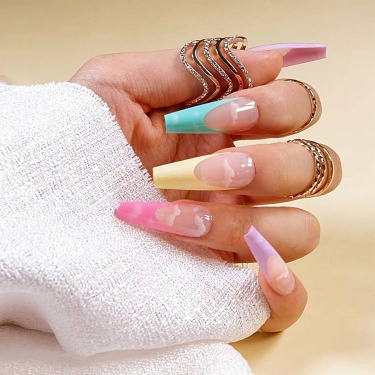 Mão com unhas arco-íris LGBTQIA+:  Polegar:  nude com francesinha lilás pastel e nuvens Indicador: nude com francesinha verde pastel e nuvens Médio: nude com francesinha amarelo pastel e nuvens Anelar: nude com francesinha rosa pastel e nuvens Mínimo nude com francesinha lilás pastel e nuvens