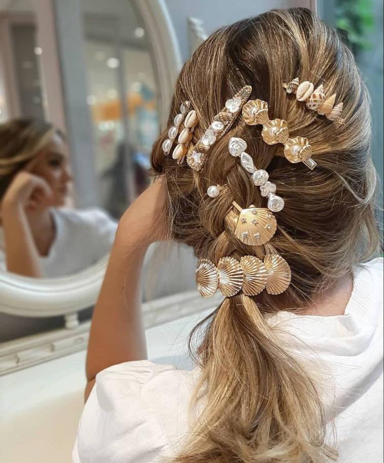 Mulher de pele clara com cabelo loiro preso com acessórios de conchas e búzios