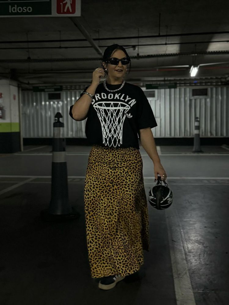 Mulher de pele clara de blusa preta de basquete e saia midi de onça 