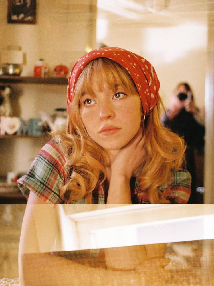 Sydney Sweeney usando blusa xadrez e bandana vermelha no cabelo solto 