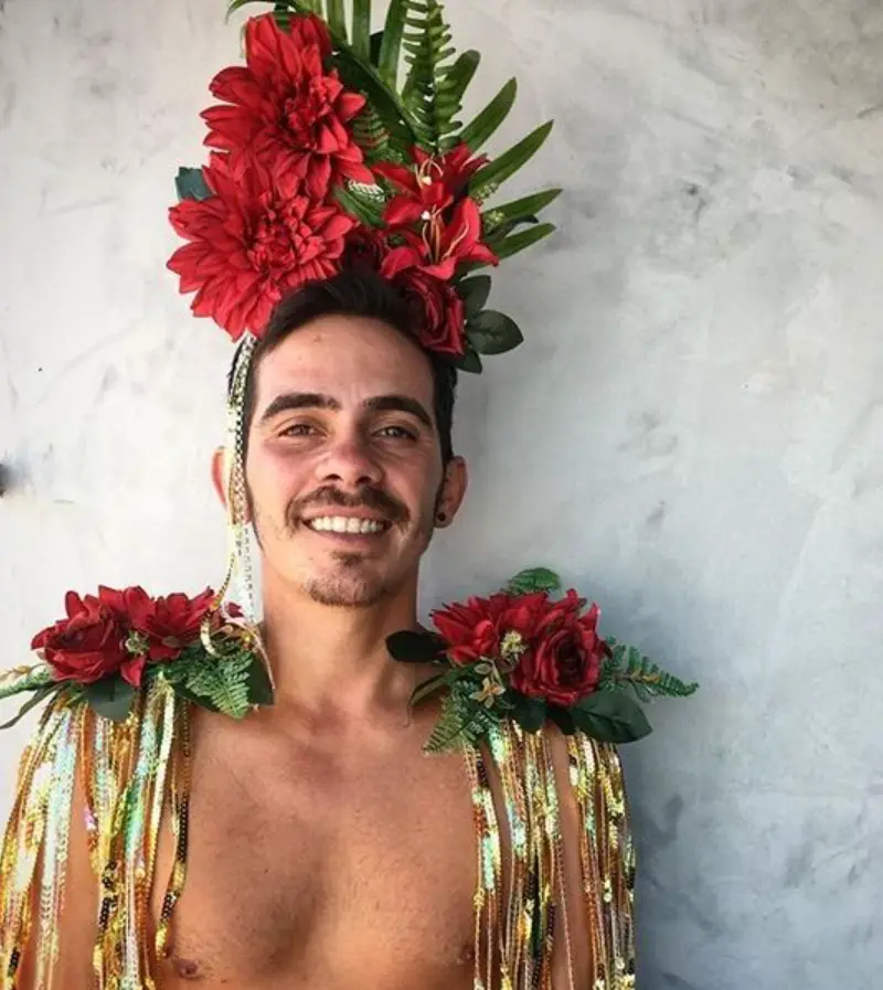Homem de pele clara com tiara e ombreira de flores